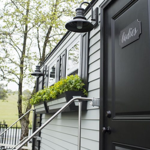 Black Tie Luxury restroom trailers exterior with vinyl siding, light fixtures, flower boxes, windows and dark trim